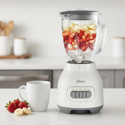 Oster 6-cup glass jar smoothie blender filled with fruit, shown next to a standard coffee mug for scale.