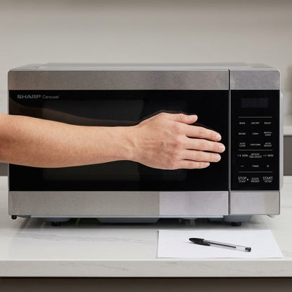 Scale reference of the Sharp SMC0985KSC 0.9 cu. ft. microwave shown beside a hand and pen for size.