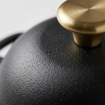 Macro detail of the Tramontina Bread Oven's textured black enamel finish and brushed gold knob.
