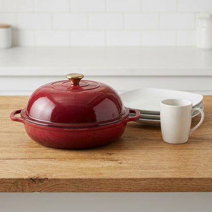 Tramontina Cranberry Red 9.5-inch bread oven beside a coffee mug and plates for scale on a table.
