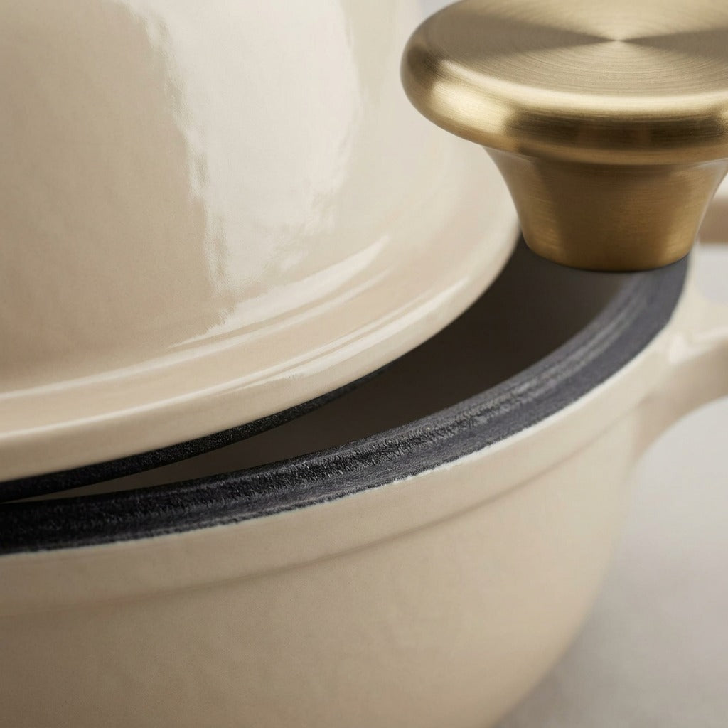 Macro detail of Tramontina Bread Oven latte enamel, cast iron rim, and brushed gold knob.
