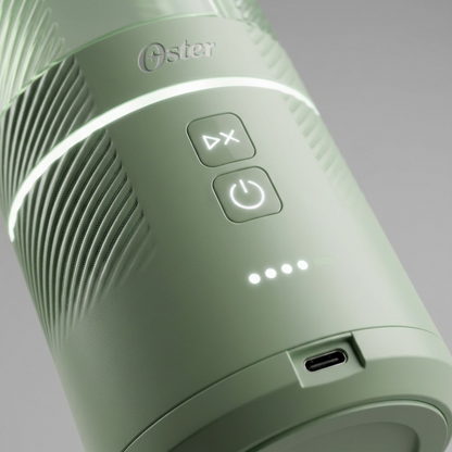 Person pressing start on a Matcha Green Oster GoMAX Portable Blender charging on a kitchen counter.